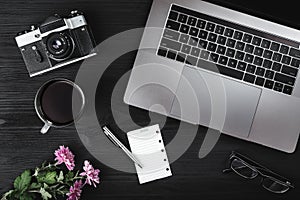 Office desk workplace. Cup of tea or coffee, photo camera, laptop computer, eyeglasses and green pink plant on old wood table. Top