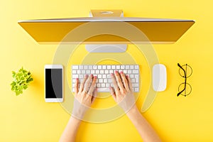 Office desktop concept. Womanâ€™s hands working on computer with business accessories on yellow background.