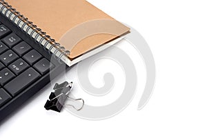 Office desktop with group of Black metal binder paper clip clamps, keyboard and note book isolated on white - image