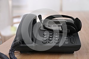 Office desktop telephone and headset on wooden table. Hotline service