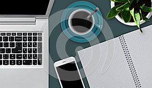 Office desktop with various objects. Laptop, cup of coffee or tea, smartphone and blank notebook laying on office desk. Workspace