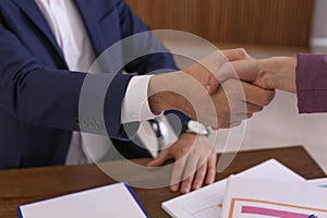 Office employees shaking hands over table with documents