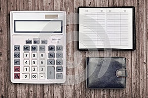 Office flat lay composition with calculator, address book and black purse on brown wooden table background with top view.