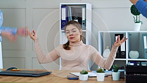 Office girl meditating at workplace and ignoring irritated colleagues