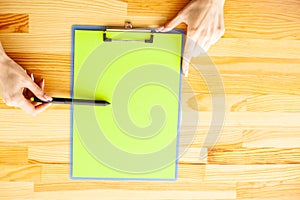 Office Hand Holding a Folder with a Green Color Paper on the Background of the Wooden Table. Copyspace. Place for Text.