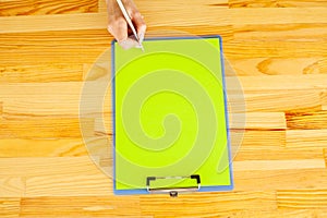 Office Hand Holding a Folder with a Green Color Paper on the Background of the Wooden Table. Copyspace. Place for Text.
