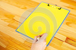Office Hand Holding a Folder with a Yellow Color Paper and Pen on the Background of the Wooden Table. Copyspace. Place for Text.