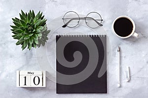 Office or home table desk. Wooden cubes calendar May 10. Black notepad, cup of coffee, succulent, glasses on marble background