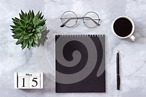 Office or home table desk. Wooden cubes calendar May 15. Black notepad, cup of coffee, succulent, glasses on marble background