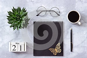 Office or home table desk. Wooden cubes calendar May 21. Black notepad, cup of coffee, succulent, glasses on marble background