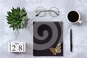 Office or home table desk. Wooden cubes calendar May 28. Black notepad, cup of coffee, succulent, glasses on marble background