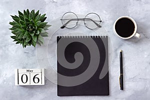Office or home table desk. Wooden cubes calendar May 6th. Black notepad, cup of coffee, succulent, glasses on marble background