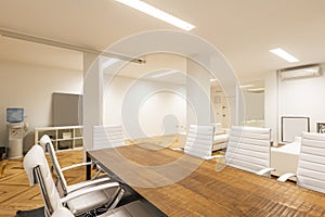 An office with an industrial-style wooden meeting table with swivel chairs upholstered in white leatherette