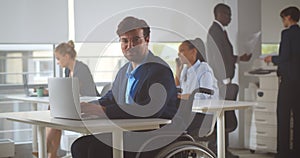 Office manager looking at camera sitting in modern startup company office in wheelchair