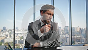 Office manager reading documents at panoramic window. Calm man drinking coffee