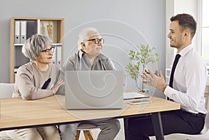 In office realtor advises happy elderly pensioners on real estate purchases. Needs of pensioners broker guides through photo