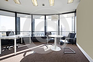 Office with a small white round table next to a large window with views, a rectangular table, carpeted floors, curved walls and a