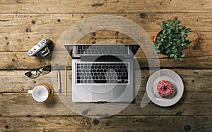 Office stuff with photo camera, laptop and coffee cup, donut, plant top view shot, with copyspace for your individual text