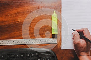 Office suply with hand holding pen in white paper with clip ruler and computer keyboard wooden