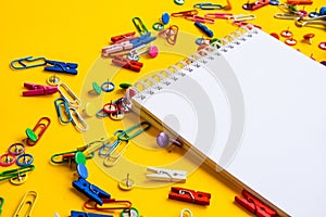 Office supplies of colored buttons and paper clips with empty note pad with copy space on yellow background