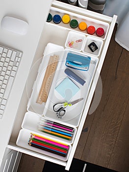 Office supplies are laid out in a white plastic container in the shelf of the desk. Back to school.