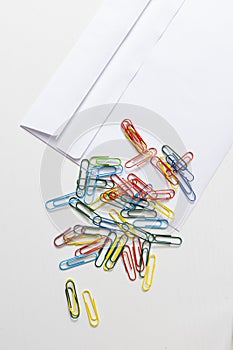 Office supplies, white envelope, colorful paper clips lying on white table