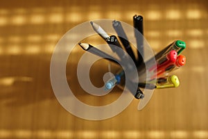 Office supplies on a wooden table. Colored pencils and ballpoint pens in a stand. Selective focus