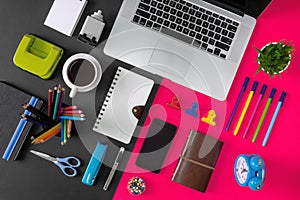 Office supply items, laptop and coffee on black and pink background.