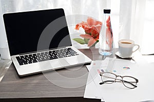 Office table with blank screen on laptop and beautiful flower ,