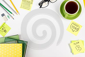 Office table desk with green supplies, blank note pad, cup, pen, glasses, crumpled paper, magnifying glass, flower on