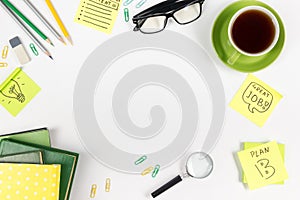 Office table desk with green supplies, blank note pad, cup, pen, glasses, crumpled paper, magnifying glass, flower on