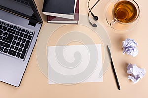 Office table desk with set of colorful supplies, white blank note pad, cup, pen, pc, crumpled paper, flower on beige