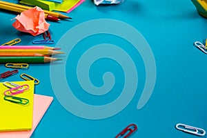 Office table desk with set of colorful supplies, white blank note pad, cup, pen, pc, crumpled paper, flower on blue