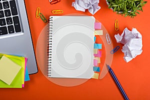 Office table desk with set of colorful supplies, white blank note pad, cup, pen, pc, crumpled paper, flower on red