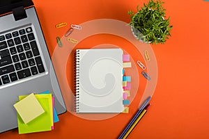 Office table desk with set of colorful supplies, white blank note pad, cup, pen, pc, crumpled paper, flower on red