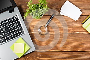 Office table desk with set of colorful supplies, white blank note pad, cup, pen, pc, crumpled paper, flower on wooden