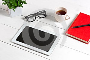 Office table desk with set of supplies, red notepad, cup, pen, tablet, glasses, flower on white background. Top view