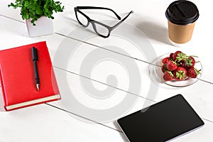 Office table desk with set of supplies, red notepad, cup, pen, tablet, glasses, flower on white background. Top view
