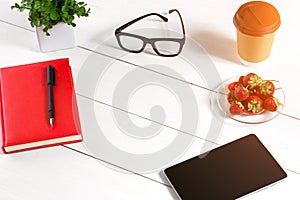 Office table desk with set of supplies, red notepad, cup, pen, tablet, glasses, flower on white background. Top view