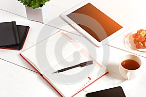 Office table desk with set of supplies, white blank notepad, cup, pen, tablet, flower on white background. Top view