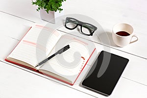 Office table desk with set of supplies, white blank notepad, cup, pen, tablet, glasses, flower on white background. Top