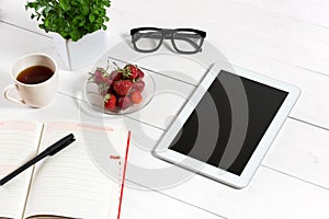 Office table desk with set of supplies, white blank notepad, cup, pen, tablet, glasses, flower on white background. Top