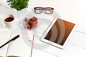 Office table desk with set of supplies, white blank notepad, cup, pen, tablet, glasses, flower on white background. Top