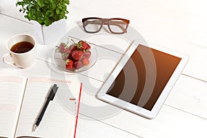 Office table desk with set of supplies, white blank notepad, cup, pen, tablet, glasses, flower on white background. Top