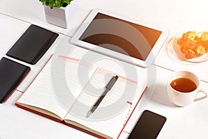 Office table desk with set of supplies, white blank notepad, cup, pen, tablet, glasses, flower on white background. Top