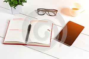 Office table desk with set of supplies, white blank notepad, cup, pen, tablet, glasses, flower on white background. Top