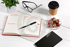 Office table desk with set of supplies, white blank notepad, cup, pen, tablet, glasses, flower on white background. Top