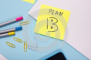 Office table desk with supplies, blank note pad, cup, pen, pc, crumpled paper, flower on blue background. Top view