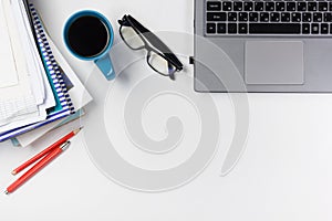 Office table desk with supplies, blank note pad, cup, pen, pc, crumpled paper, flower on white background. Top view