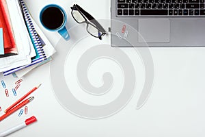 Office table desk with supplies, blank note pad, cup, pen, pc, crumpled paper, flower on white background. Top view